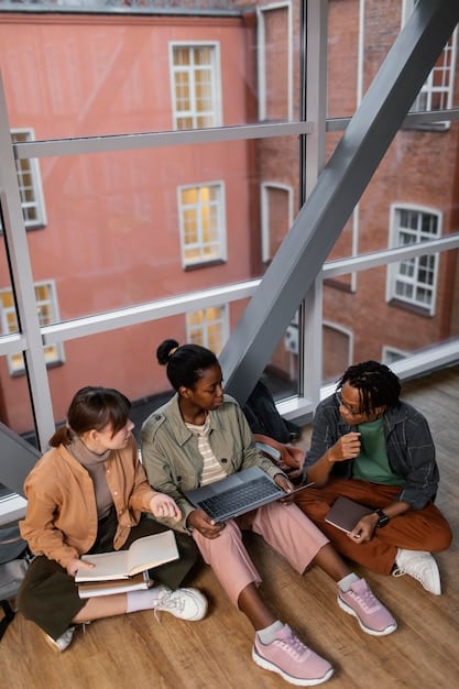 An image showing a diverse group of students studying together in a modern library or study hall. The setting is collaborative, with students using laptops, books, and engaging in discussions, reflecting the environment that 529 plans help to fund.
